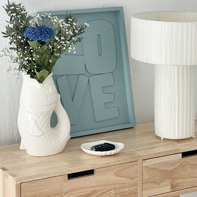 Vase céramique en forme de poisson blanc avec un bouquet à l'intérieur posé sur un bureau 