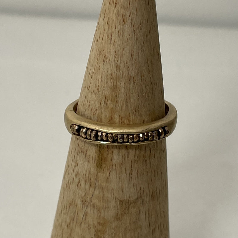 Bague alliance talisman dorée sur un cône en bois et devant un fond blanc 