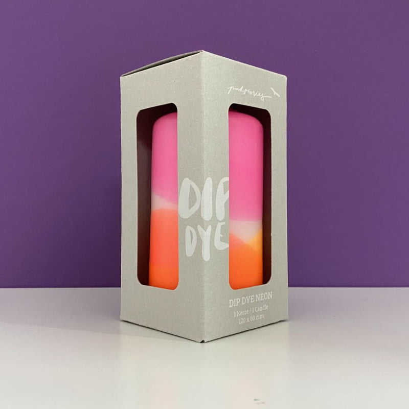 Bougie fluo rose et orange dans son emballage devant un fond violet