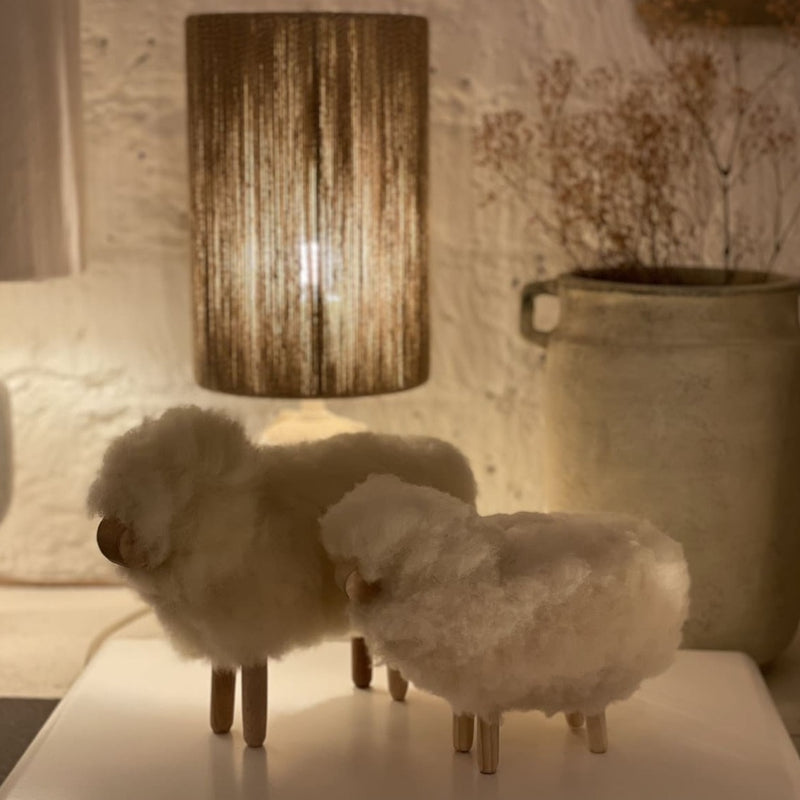 Moutons en laine et bois devant fond lumineux blanc avec une lampe et un pot 