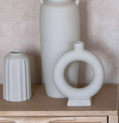 Vase en céramique gris devant un fond rosé et des objets gris