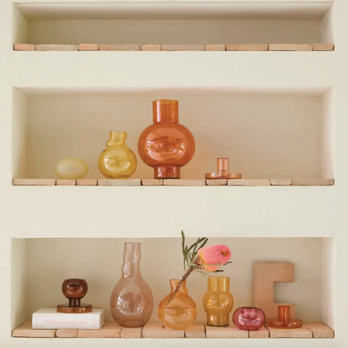 Étagères en brique incrustées dans un mur blanc sur lesquelles sont posés es vases et des bougeoirs dans les tons roses et jaunes