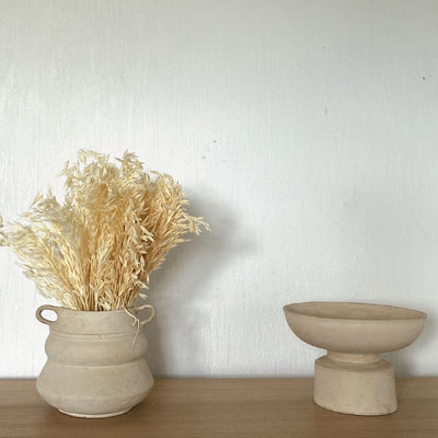 Vase et coupe beiges posés sur un support en bois clair