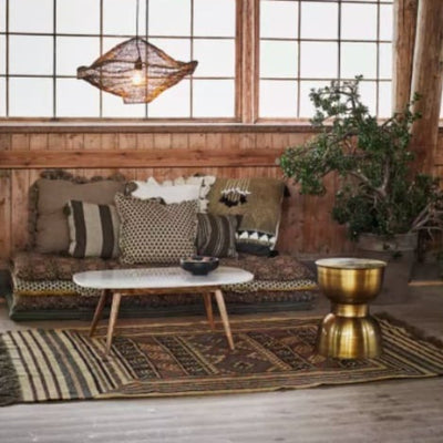 Salon dans lequel on trouve une banquette de matelas et coussins, une table basse blanche et un tabouret, le tout posé sur un tapis oriental