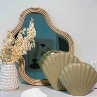 Vases en formes de coquillage, vase blanc et miroir asymétrique posés sur un rebord blanc