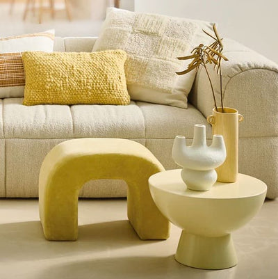 Salon avec un canapé blanc cassé, tabouret et table ronde sur laquelle sont posés des vases