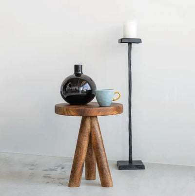 Table en bois ronde avec trois pieds sur laquelle est posée une tasse colorée et un vase noir
