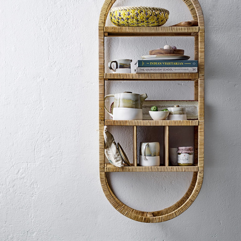 Etagère murale en rotin sur laquelle sont posés des objets de décoration et de la vaisselle