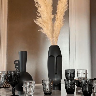 Assortiment de verres visage posés sur une table en marbre à côté de vases noirs